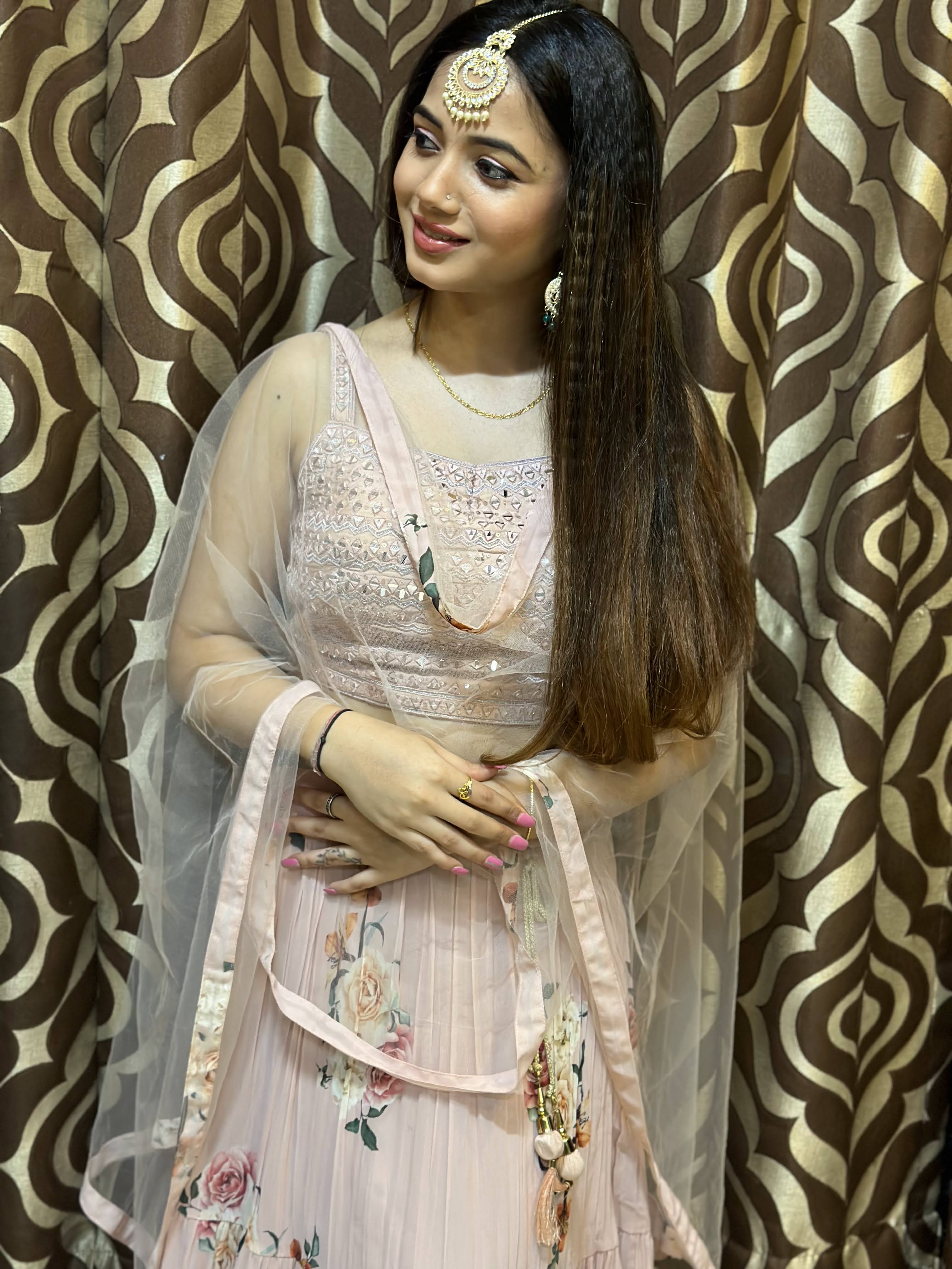 Young woman with long, dark, straight, and shiny hair, wearing a pink floral lehenga and traditional maang tikka and earrings, smiling gracefully. Her skin appears smooth and radiant.